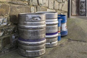 Two silver metal beer kegs against an outside wall