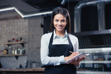 Charming female waiter in apron writing order