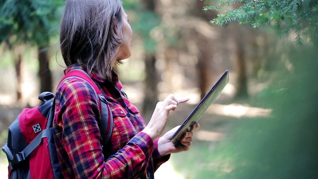 Lost, frightened woman looking for direction on tablet in the forest
