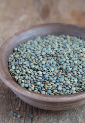 Dry green french lentils (Du Puy) in a clay bowl on wooden table