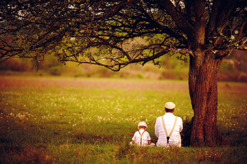 father and son sitting under the tree on spring lawn