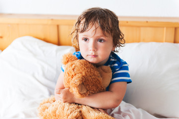 Cute toddler boy resting in a bed with teddy bear