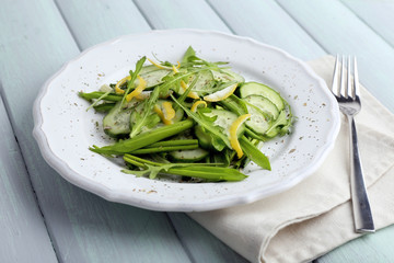 Green salad with cucumber, arugula and lemon peel on wooden background