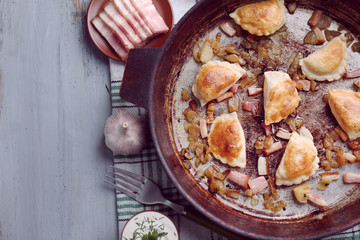 Fried dumplings with onion and bacon in frying pan, on wooden table background