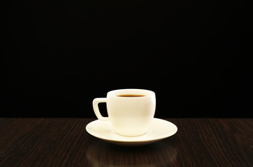 Cup of coffee on wooden table, on dark background