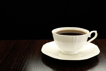 Cup of coffee on wooden table, on dark background