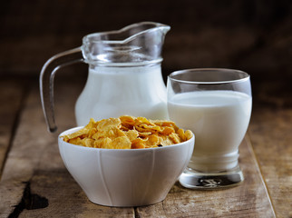 cornflakes in bowl and glass of milk on wooden table