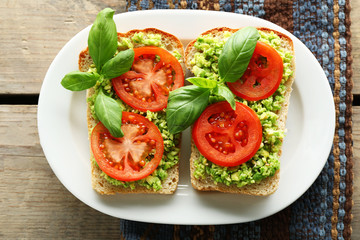 Vegan sandwich with avocado and vegetables on plate, on wooden background