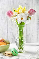 Spring bouquet in vase and tasty macaroons on color wooden background