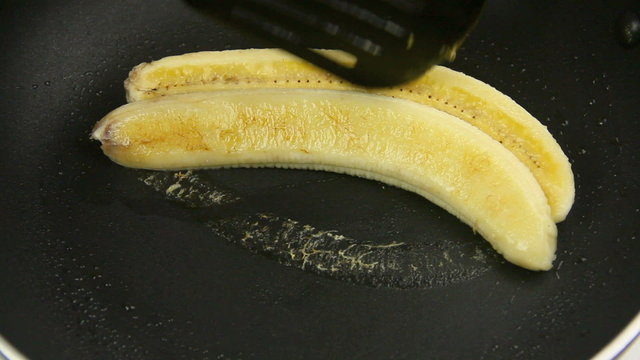 Banana being put into a pan with a spatula to fry.
