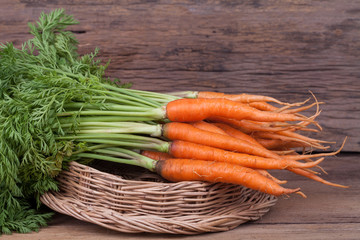 Bunch of fresh carrots with green leaves over wooden background