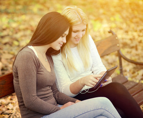 Two young women looking at tablet and chating online with friend