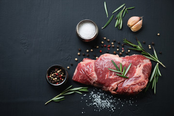 Oben Blick auf rohes Ribeye-Steak mit Gewürzen auf schwarzem Hintergrund