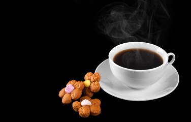 A cup of hot coffee and cookies isolated on a black background.