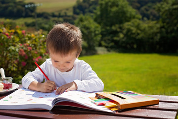 Adorable boy, drawing a painting in a book, outdoor