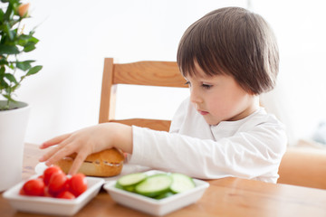 Obraz na płótnie Canvas Beautiful little boy, eating sandwich at home, vegetables on the