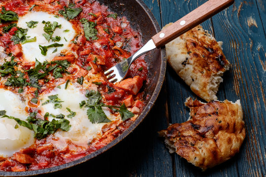 Fried eggs in a frying pan with tomatoes, sausage and greens