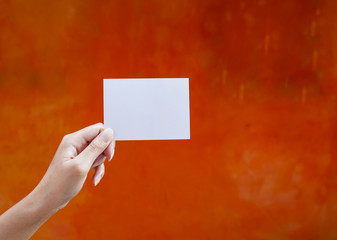 Hand holding white empty card with space on orange wall