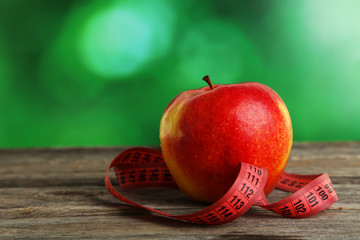 Red apple with measuring tape on grey wooden background
