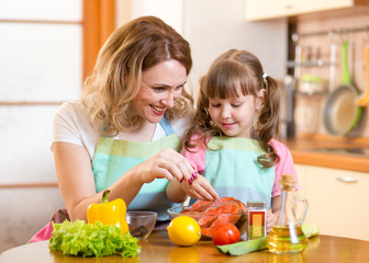 Cute woman with child daughter preparing fish in kitchen