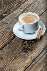 Cup of coffee on amid whole coffee beans with cinnamon