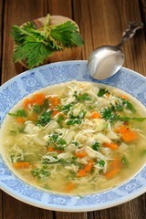 Nettle soup with eggs in blue plate with fresh nettle and spoon