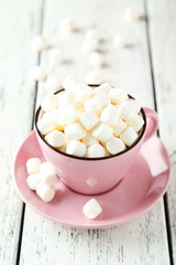 Fototapeta na wymiar Marshmallows in pink cup on white wooden background