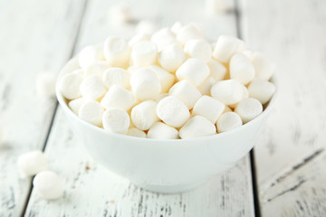 Marshmallows in bowl on white wooden background