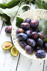 Fresh plums in basket on white wooden background