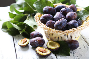 Fresh plums in basket on white wooden background