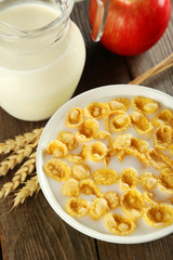 Bowl of cornflakes with milk on brown wooden background