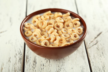 Bowl of cornflakes with milk on white wooden background