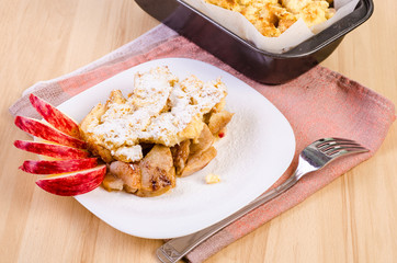 apple pie on a white plate decorated with raw apples on a wooden background