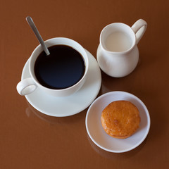 Cup of coffee, creamer jug and muffin on reflective table