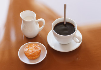 Cup of coffee, creamer jug and muffin on reflective table