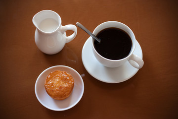 Cup of coffee, creamer jug and muffin on reflective table