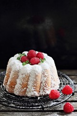Vanilla cake with fresh raspberries on a rustic dark background 