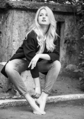 Sexy blond woman in trendy jeans and black jacket sitting barefo