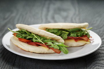 two sandwiches with ham arugula and tomatoes in pita bread on