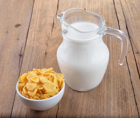 tasty cornflakes in white  bowl and glass of milk on wooden tabl