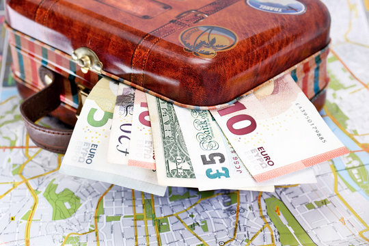 Suitcase with various money on a map.Travel concept