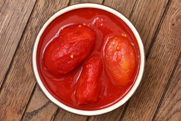 Whole canned tomatoes in pottery dish from above on wood.