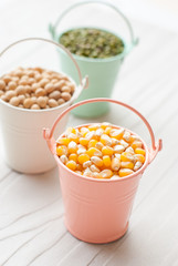 Bulk of corn grains, soy pods, mung beans in bucket on white woo