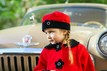 Cute little girl dressed in retro coat posing near oldtimer car