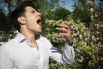 Attractive young man next to flowers sneezing