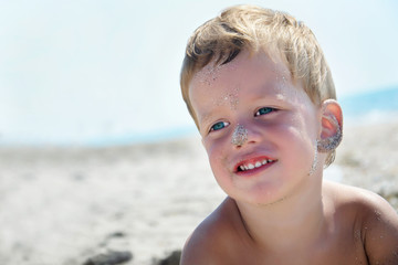 Portrait of three years boy on beach, face in sand