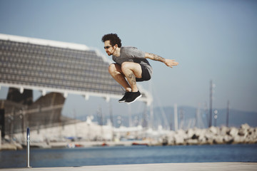 Young tracer athlete jumping over building roof against blue sky