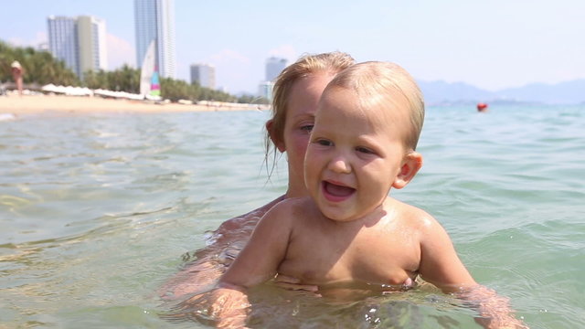 young blonde mother bathes little daughter in sea	