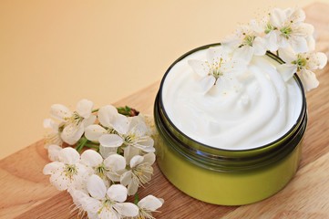 white skin care cream in jar with flowers