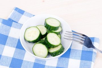 Cucumber salad in a white bowl on the bowl is fork, top view